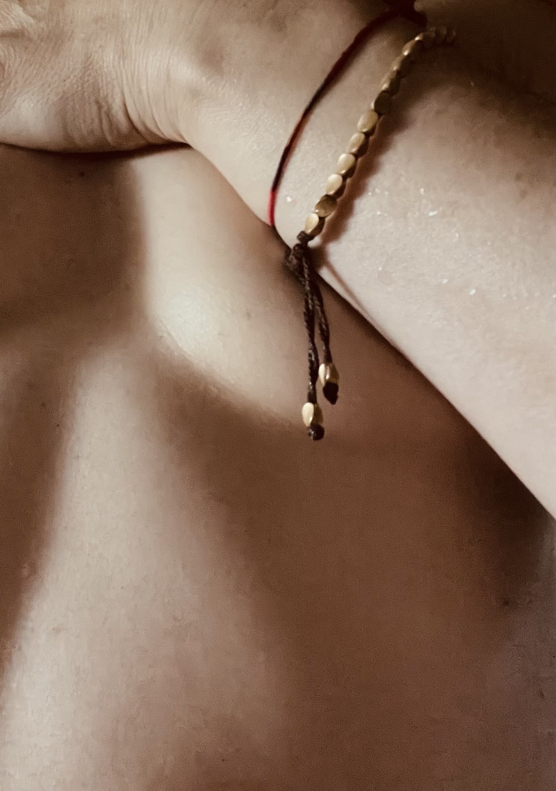 Goldfuchs left arm covering chest, water droplets reflecting light, copper necklace and Milanese bracelet visible.